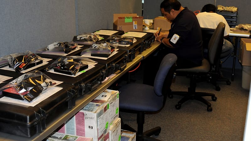 A shipping desk with a clipboard of forms, a roll of tape and stacked cartons waiting under fluorescent light.