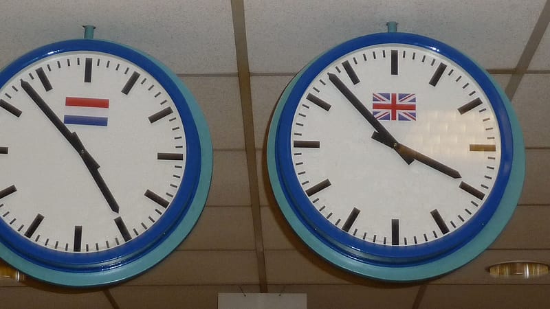 Two office telephones on a desk beside a stack of paper files and a wall clock showing a late hour.