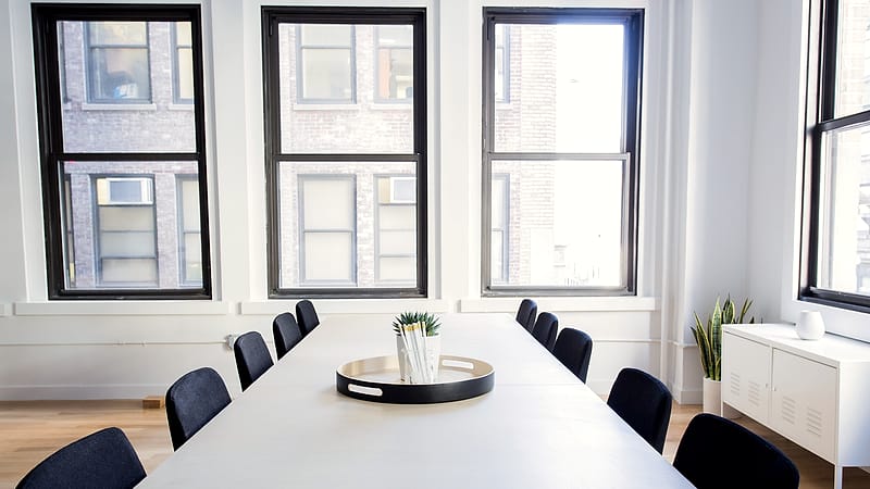 A long conference table with scattered site plans, rolled drawings, coffee cups and empty chairs beside a window.