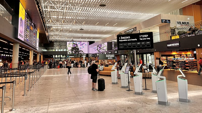 An empty airport departure hall at night with rows of seats, a lit information board and one small suitcase.